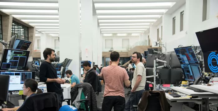 Traders talking between multi-monitor desks on the Jane Street trading floor
