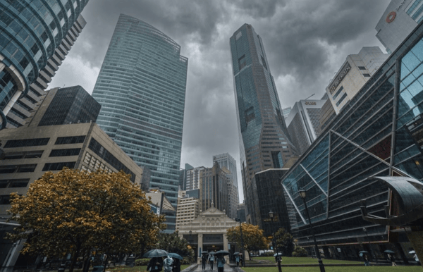 Office towers in the central business district of Singapore under a stormy sky, with people walking under umbrellas